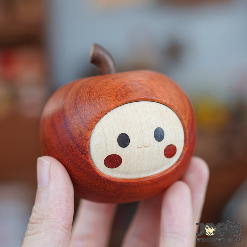 Hand holding a handcrafted wooden apple figurine with adorable expression