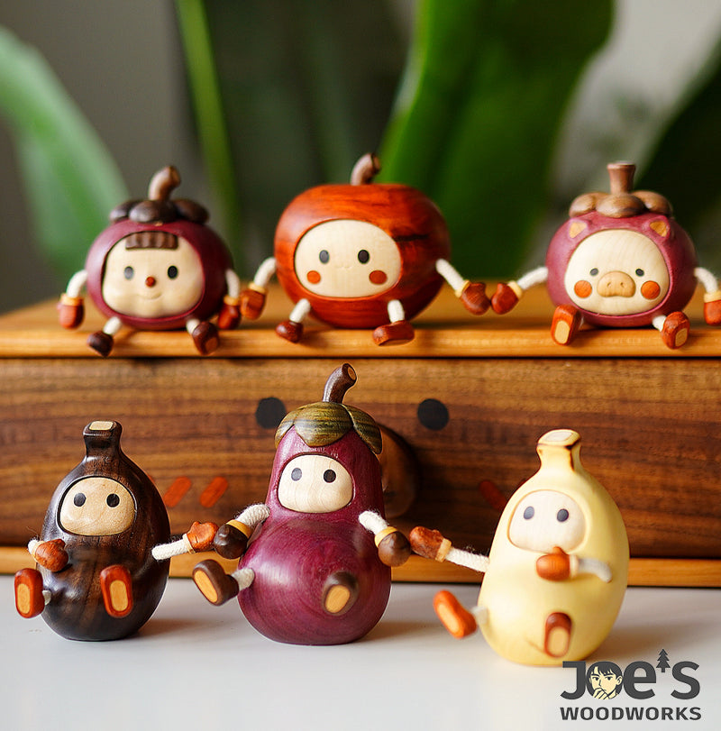 Collection of handmade wooden fruit animal figurines including pig, banana, and eggplant characters