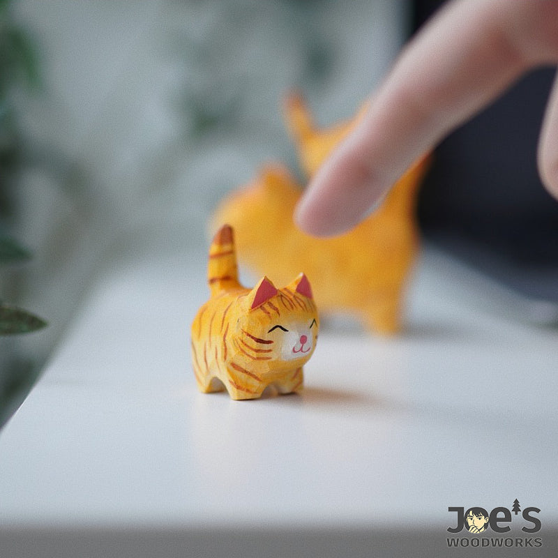 Mini handmade orange cat figurine used as cute wooden desk decor, finger touching its head