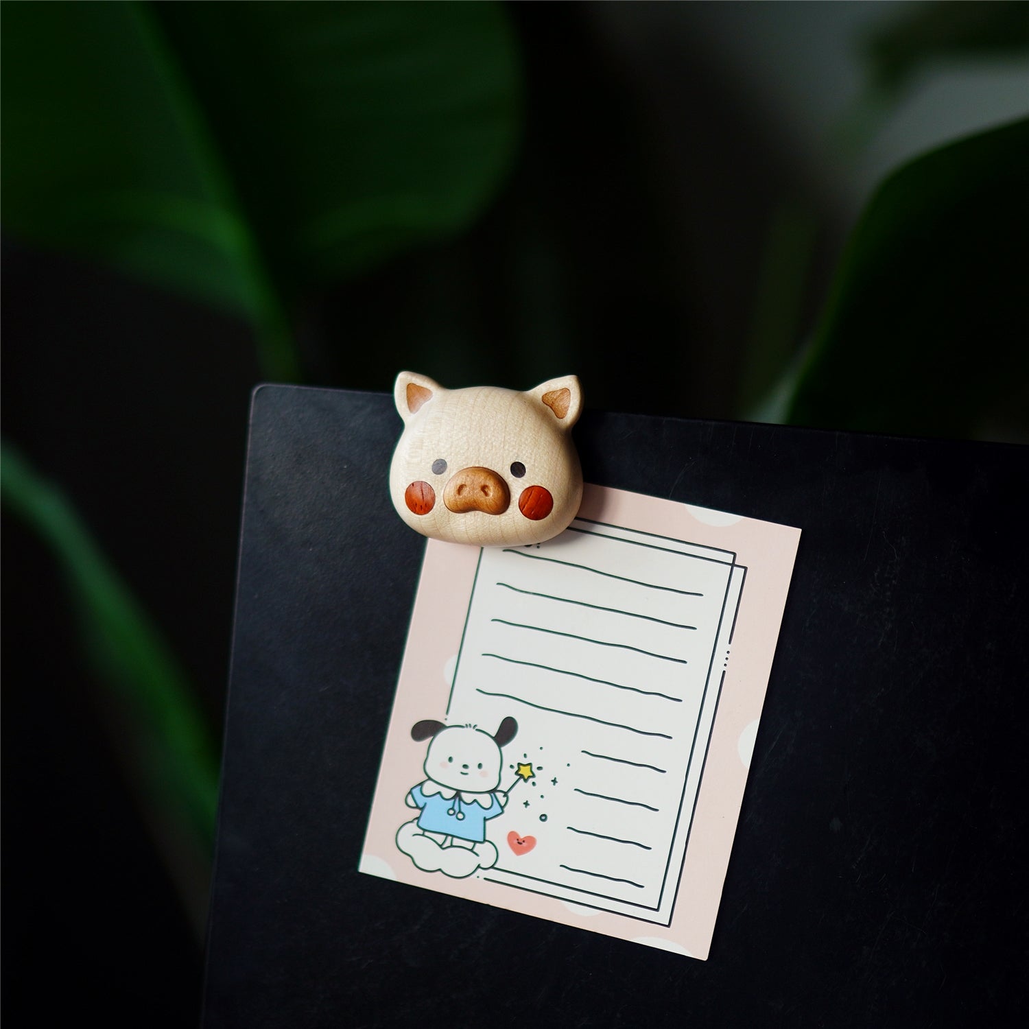 Piggy Nunu fridge magnet holding photo note on black surface, wooden pig decor