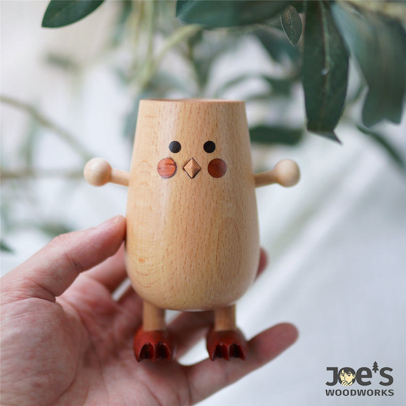 Hand holding wooden chick-shaped pen holder with adorable face design