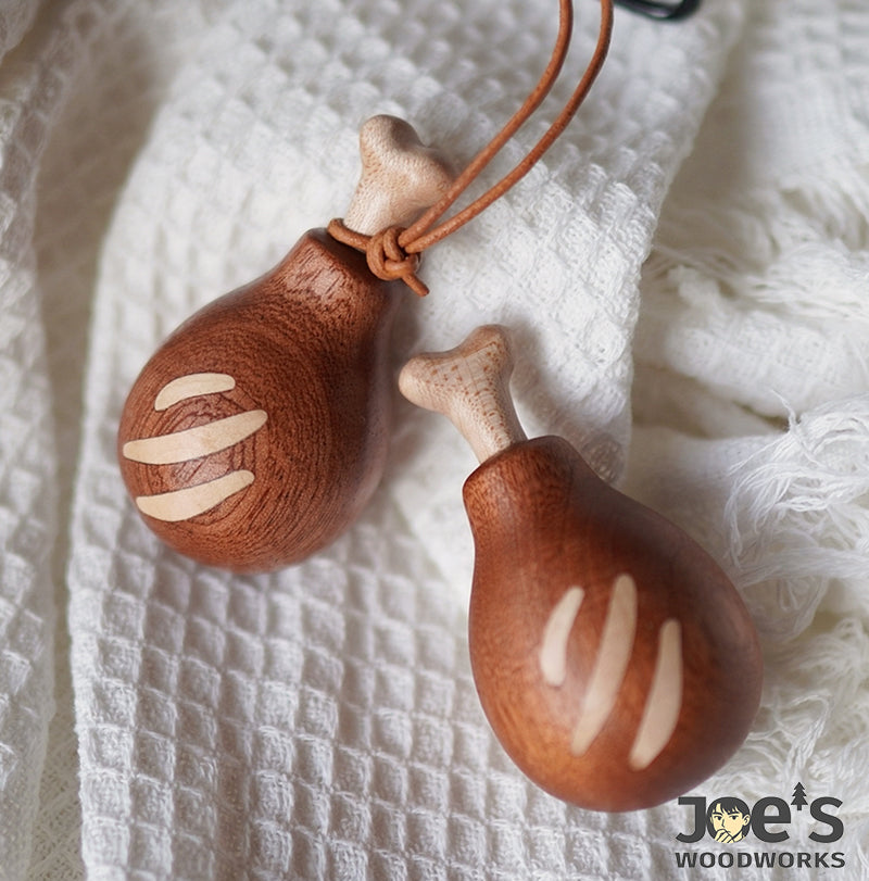 Pair of wooden drumstick keychains resting on soft white fabric, carved with stripes