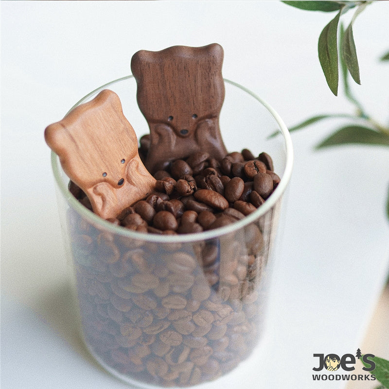 Light and dark wood fox coffee scoops resting in a glass jar of coffee beans