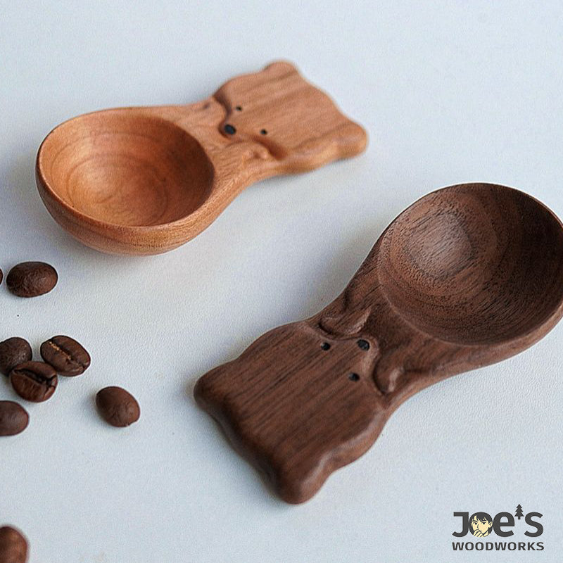 Light and dark fox-shaped wooden scoops side by side on white surface with beans