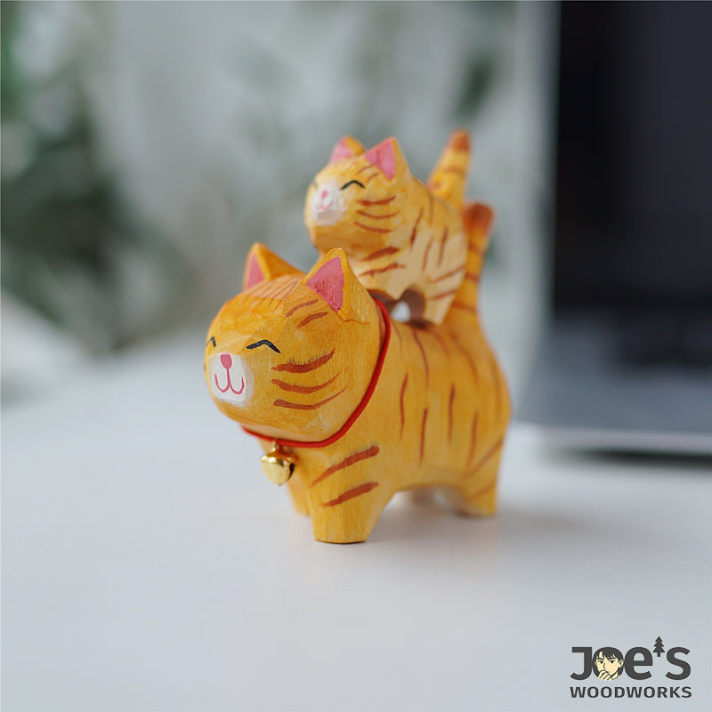 Cute parent-child orange tabby cat figurines stacked playfully, handcrafted from wood