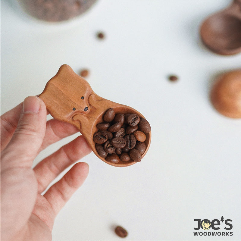 Hand holding fox-shaped wooden coffee scoop filled with whole coffee beans