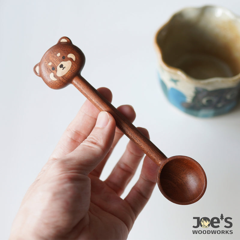 Hand holding a bear face wooden scoop, carved in warm walnut wood with fine detail.