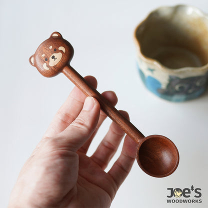Hand holding a bear face wooden scoop, carved in warm walnut wood with fine detail.