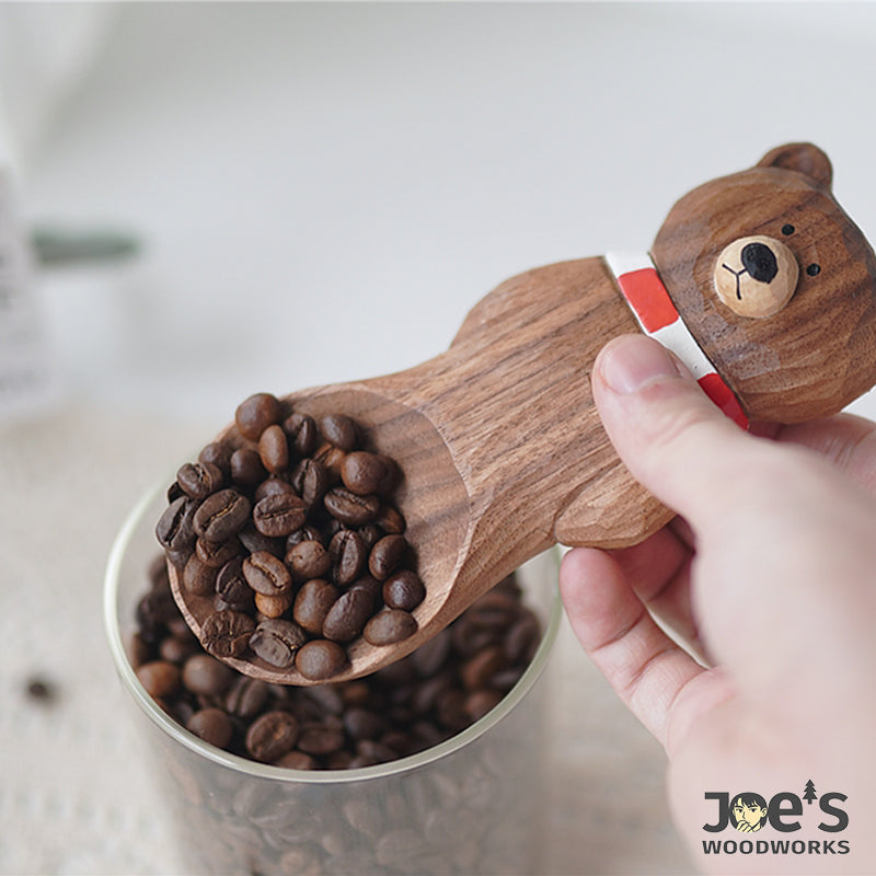 Wooden bear-shaped scoop in use, scooping roasted coffee beans from a glass jar.