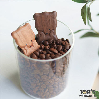 Light and dark wood fox coffee scoops resting in a glass jar of coffee beans