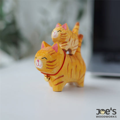 Cute parent-child orange tabby cat figurines stacked playfully, handcrafted from wood